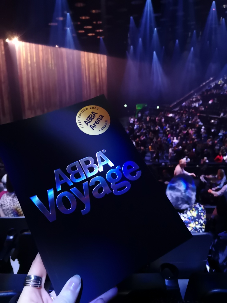 a black programme which says ABBA Voyage held up in front of a crowd of people